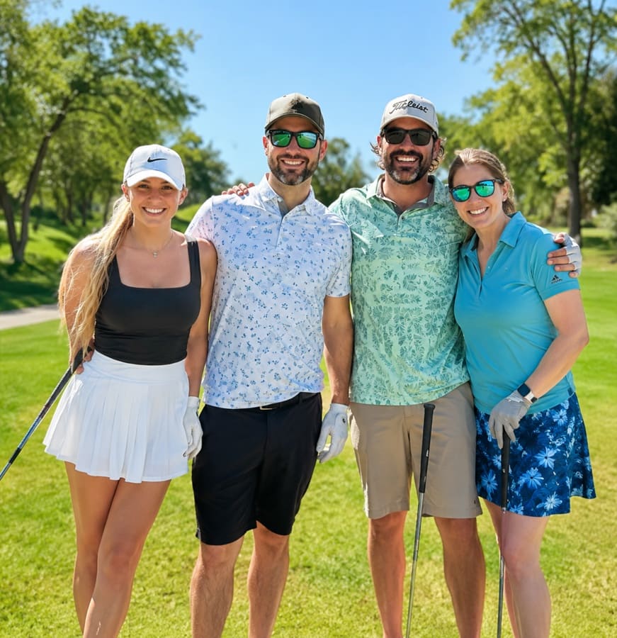 Two couples smiling together on a sunny golf course, holding their clubs