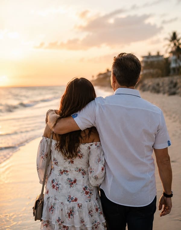 A couple walking arm in arm along the beach at sunset.